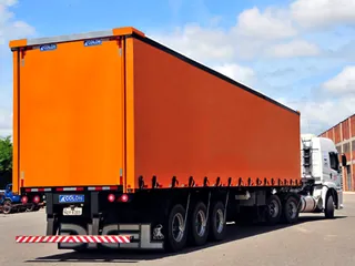 Carreta com carroceria sider laranja de cortinas fechadas