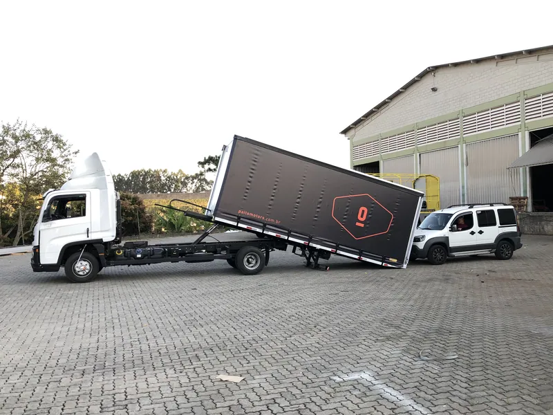 Caminhão plataforma inclinando a carroceria de cortina sider até o chão